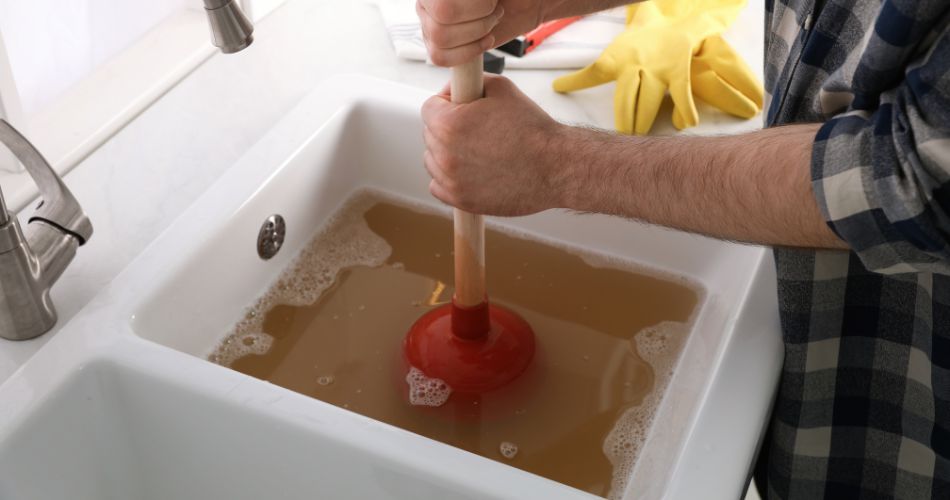 man unclogging a sink with a plunger